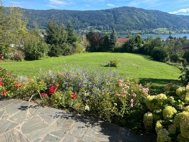 Blühender Garten mit Steinweg und Blick über den Ossiacher See