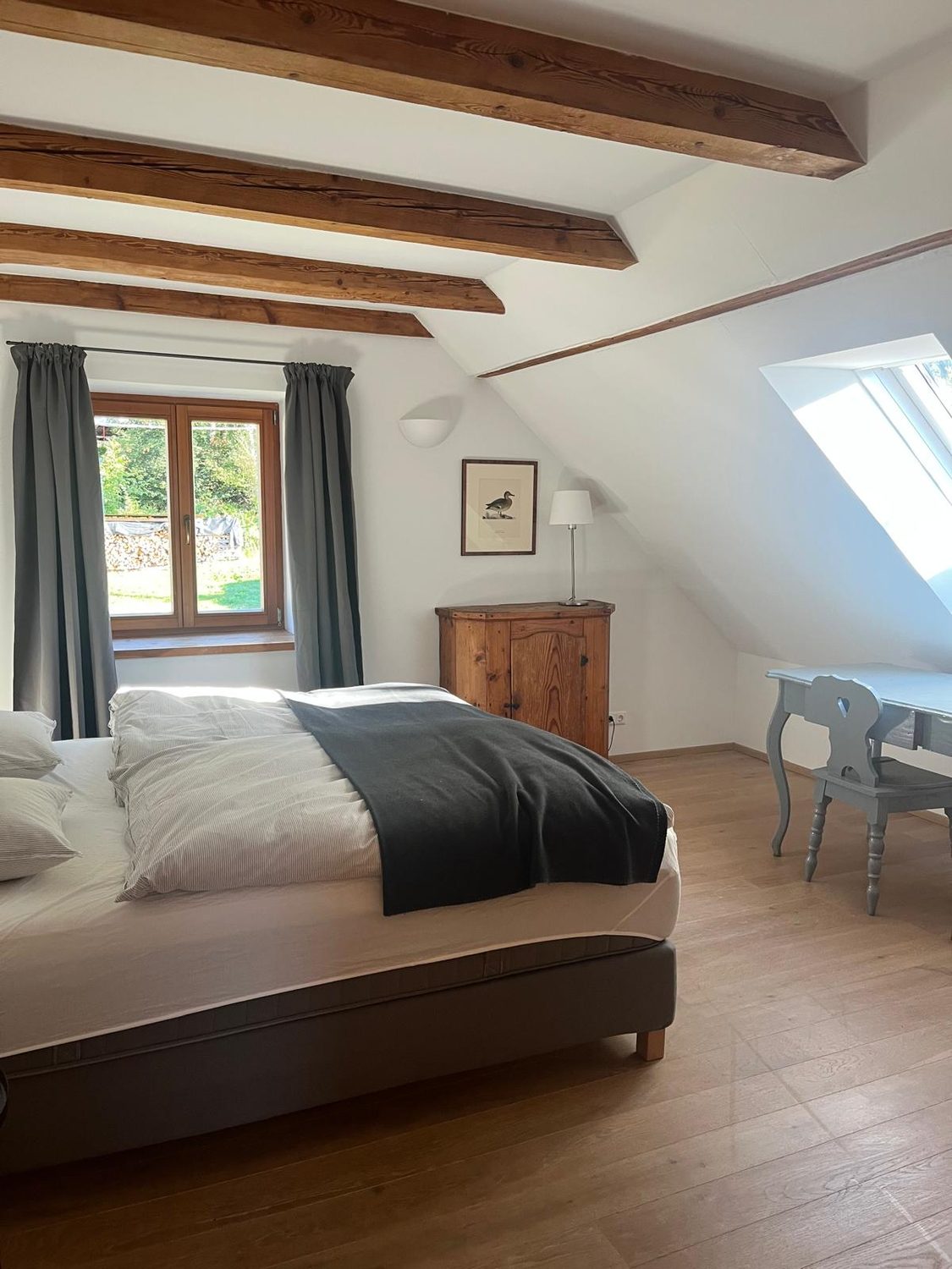 Schlafzimmer mit grauem Doppelbett unter Dachschräge und Balken