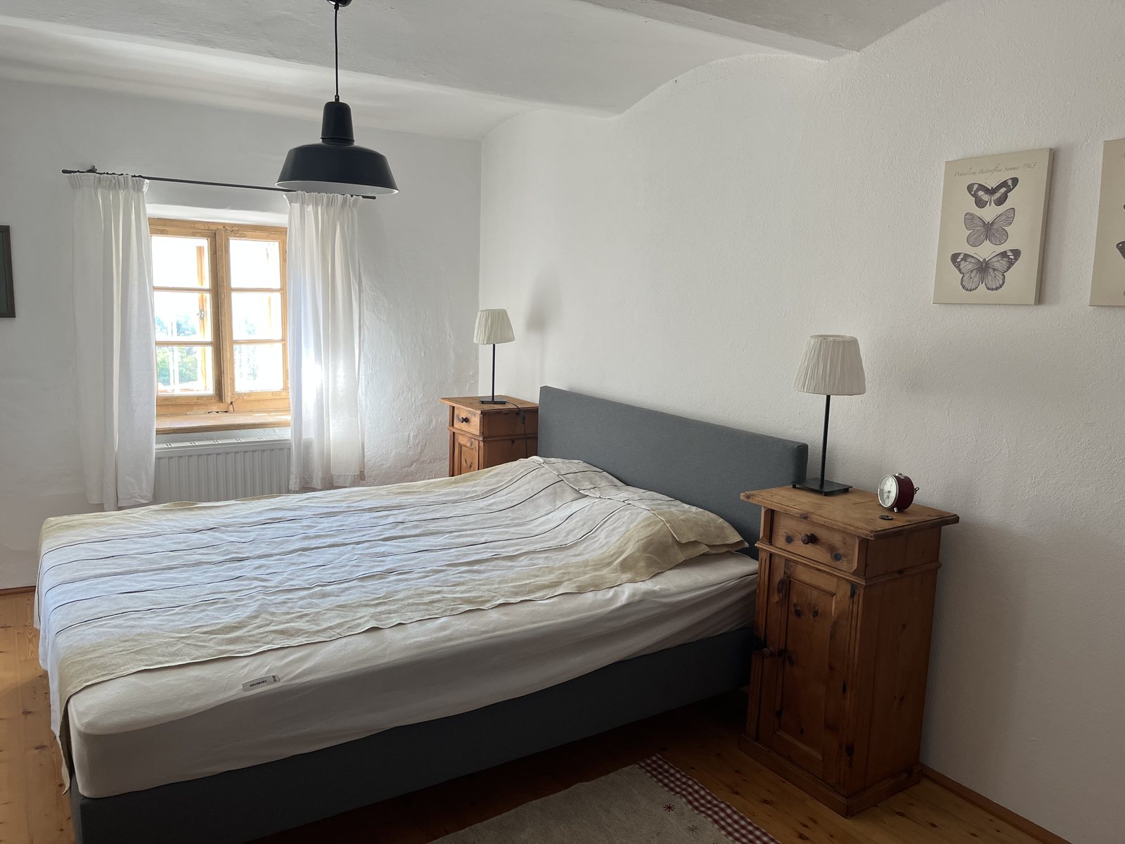 Schlafzimmer mit Doppelbett, Pinien-Nachtkästchen und Schmetterlingsbildern