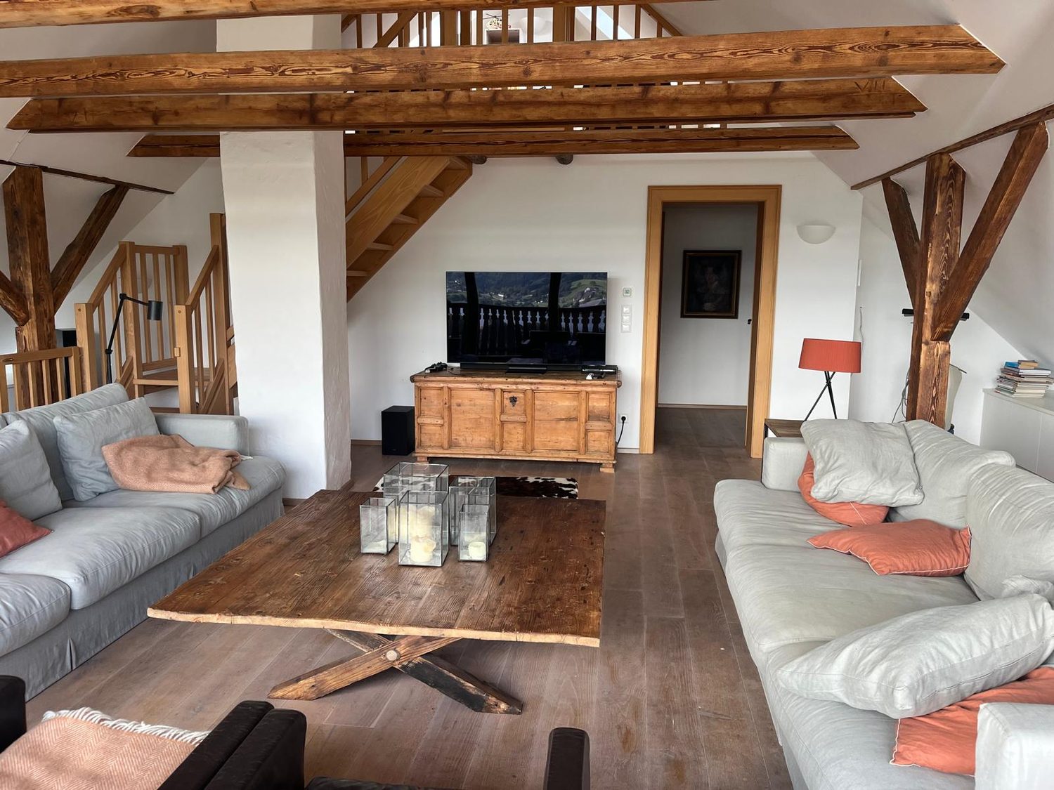 Großer Wohnraum unterm Dach mit alten Holzbalken, hellen Sofas und Massivholztisch