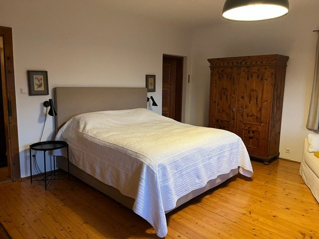 Schlafzimmer mit gepolstertem Kopfteil und antikem Bauernschrank