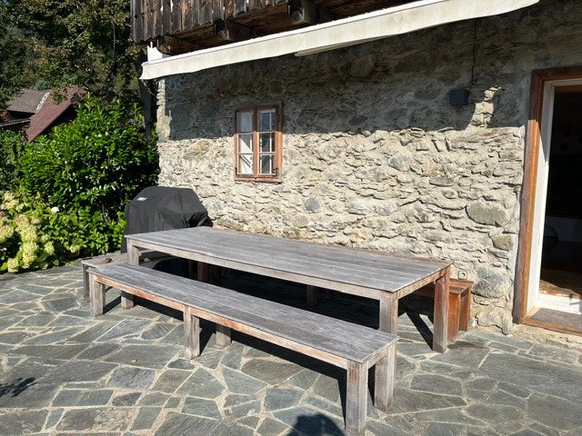 Steinterrasse mit großem Teaktisch, Bänken und Griller an der Natursteinmauer