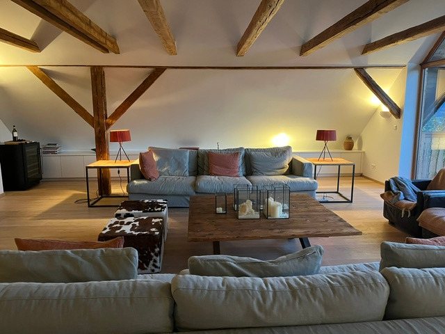 Wohnraum am Abend mit Sofas, Balkendecke und warmem Licht
