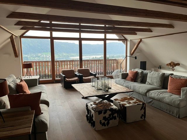 Großzügiger Wohnraum mit Balkendecke, Panoramaverglasung und Seeblick bei Tag